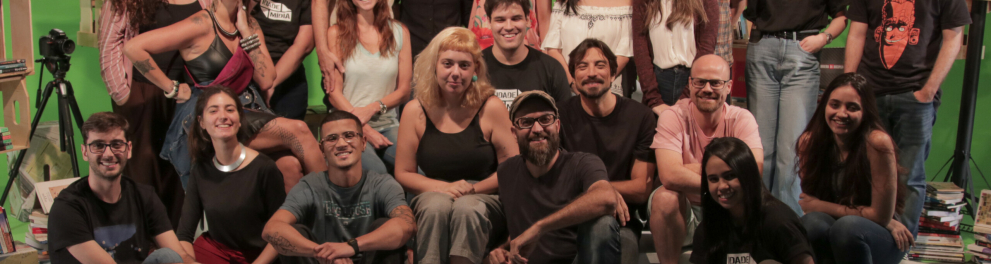 Cerca de 25 pessoas estão posando para a foto e estão no cenário do programa Idade Mídia