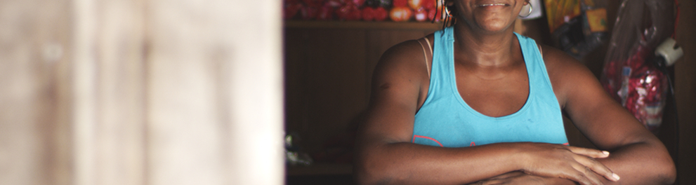 Mulher negra  de camiseta azul está com os dois braços no que parece ser uma janela ou bancada de loja