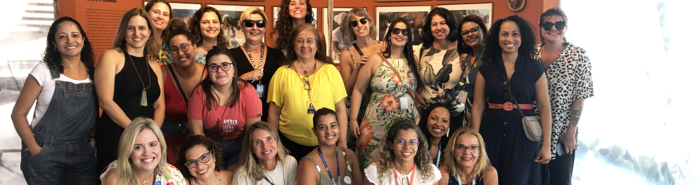 Diversas mulheres reunidas em um salão - algumas de pé (atrás), outras agachadas (à frente). Todas sorriem.