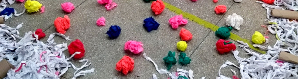 Imagem do chão com várias bolinhas coloridas de papel crepom posicionadas dentro de um círculo que foi feito com rolos de papel higiênico e papéis picotados na cor branca