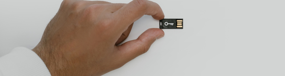 Mão masculina segurando um pen drive preto pequenino sobre um fundo completamente branco