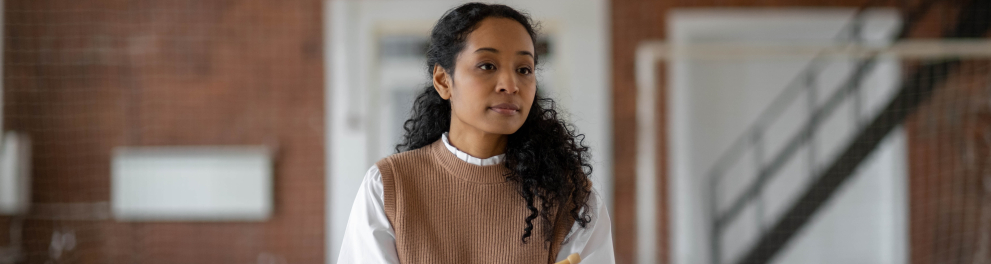 Imagem de uma mulher negra e jovem com cabelos cacheados. Ela está sentada diante de uma mesa branca com uma esfera, um objeto triangular e um livro apoiados