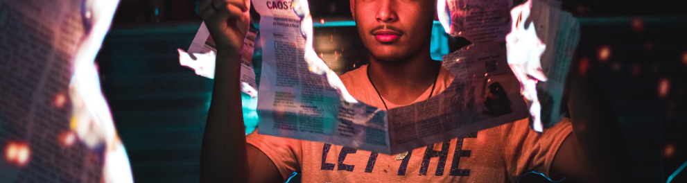 Um jovem rapaz negro está segurando um jornal em chamas com as duas mãos