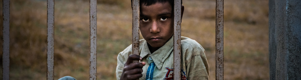 Menino de traços indianos está atrás de uma grade apresentando tristeza e melancolia