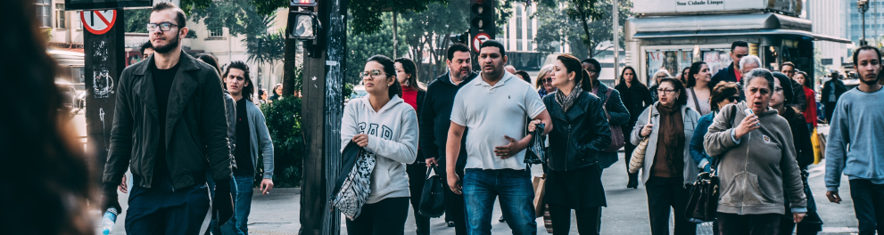 Imagem de vários pedestres atravessando uma rua larga em meio urbano