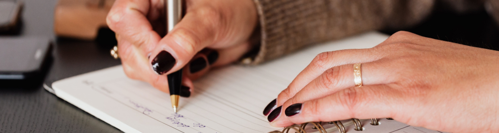 Duas mãos femininas escrevem em um caderno ou diário.