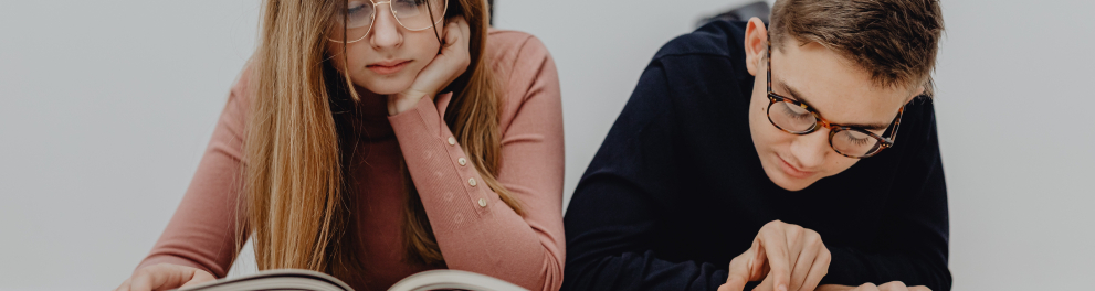 Dois adolescentes (um menino e uma menina) brancos, de óculos e que parecem ser irmãos estão lendo livros diferentes lado a lado