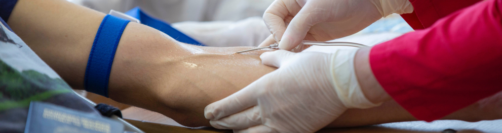imagem em close das mãos de uma enfermeira, com luvas, retirando sangue da veia uma outra pessoa