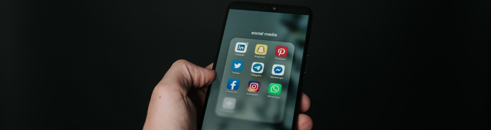 Um homem segurando um celular que mostra uma série de aplicativos de rede sociais