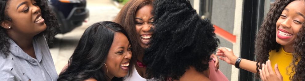 Cinco amigas negras gargalhando uma ao lado da outra ao ar livre em uma calçada