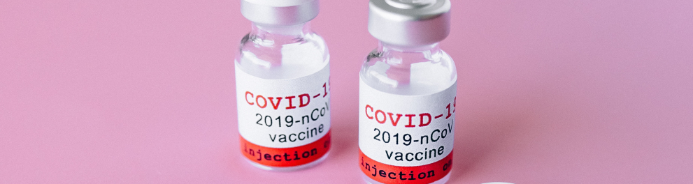 Dois frascos de vacina contra a Covid-10 em cima de uma superfície cor de rosa