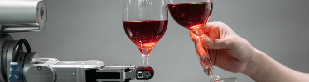 Imagem de duas taças de vinho tinto sendo brindadas, porém por uma mão humana à direita e um braço mecânico de robô à esquerda