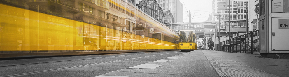 Uma locomotiva amarela foi captada em movimento enquanto há outra parada ao lado da mesma. O fundo é um meio urbano