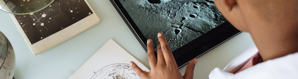 Um homem negro de camisa branca de manga comprida está mexendo em um tablet. A foto foi batida por trás e por cima do homem