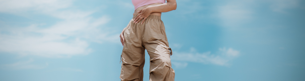 imagem de uma linda e jovem mulher posando de calça e top. Ao fundo, o céu azul com nuvens