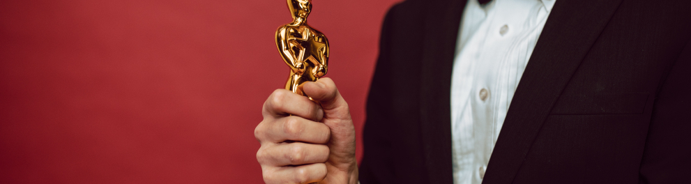 Um homem segurando um troféu dourado de base preta com as duas mãos. Ele está de terno e sua cabeça está cortada na imagem