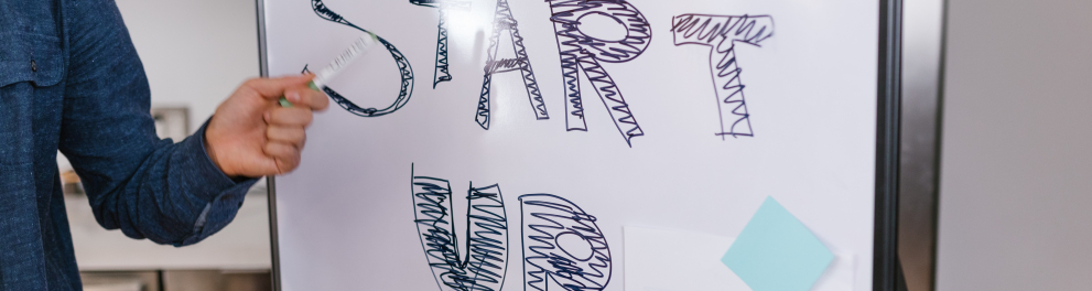 Um quadro de apresentação em reunião com as palavras START UP em letras grandes e a mão de uma pessoas apontando para tal