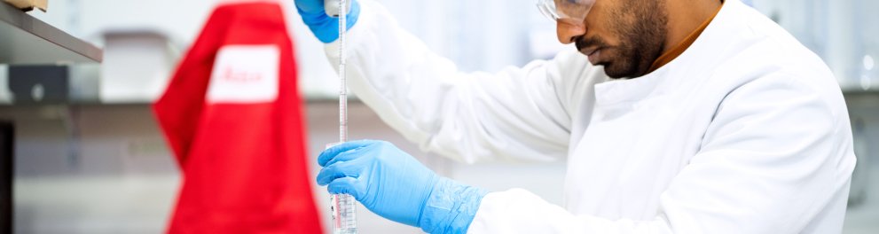 Um cientista moreno em um laboratório mexendo em um frasco e acrescentando algum líquido