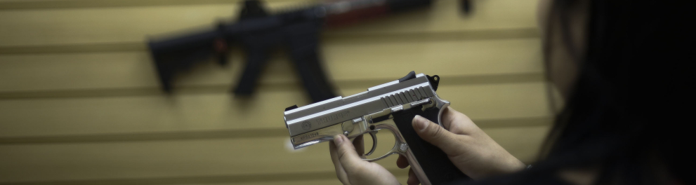 A imagem mostra algumas armas expostas e uma na mão de uma mulher