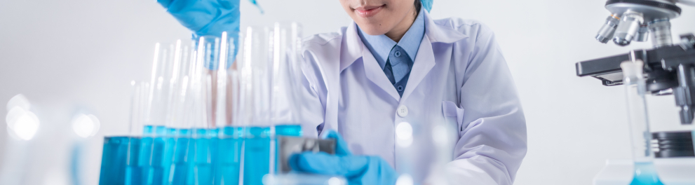 Uma cientista asiática está aplicando um líquido azul em vários recipientes cilíndricos de vidro através de um conta gotas