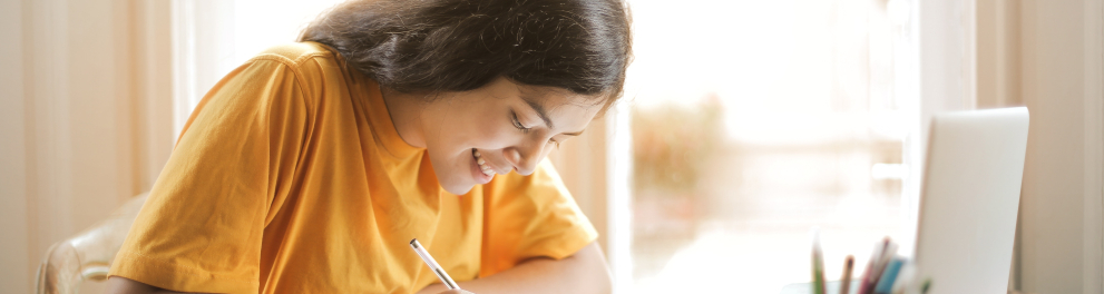 Imagem mostra uma garota sorrindo enquanto escreve em seu caderno