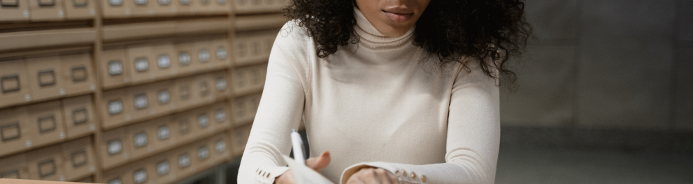 Mulher negra de cabelos cacheados e soltos está folheando um livro com um semblante de seriedade