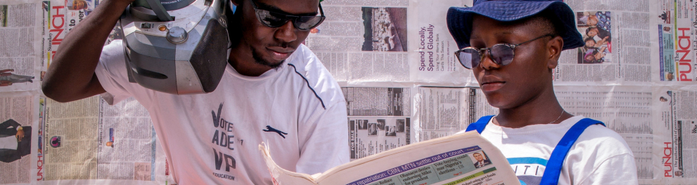 Imagem mostra duas pessoas fazendo a leitura de um jornal impresso