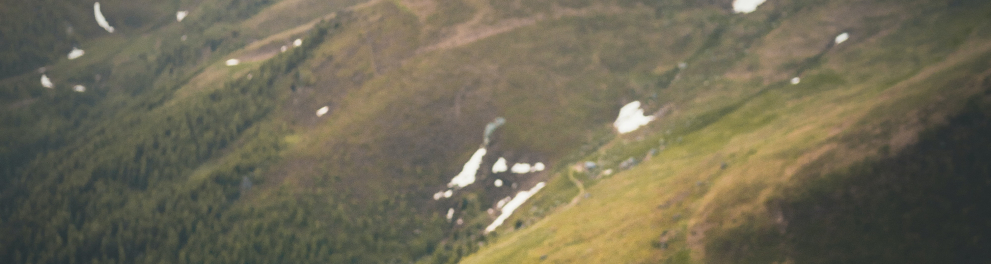 Um homem está sentado em uma rocha admirando a belíssima paisagem à sua frente, que é a de montanhas cobertas por vegetação ao ar livre. Ele está de costas para quem bateu a foto