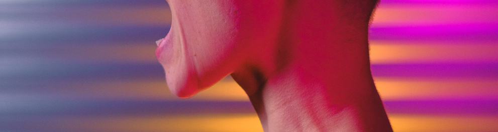 Uma mulher careca está de perfil para quem bateu a foto. Ela está de regata cor de rosa e parece estar gritando