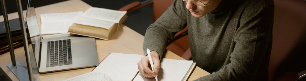 Homem sentado à mesa de escritório fazendo alguma anotação em um caderno