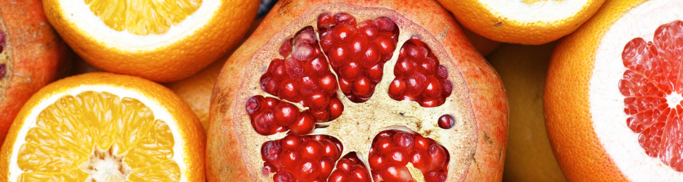 Várias frutas amontoadas e cortadas pela metade. São laranjas, amoras e toranjas