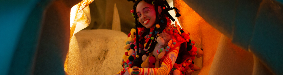 Uma menina negra sentada no que parece ser o interior de uma caverna 