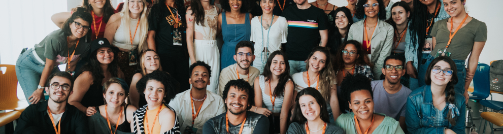 Imagem de dezenas de pessoas amontoadas e posando para uma foto. Há pessoas sentadas no chão, outra agachadas e várias em pé