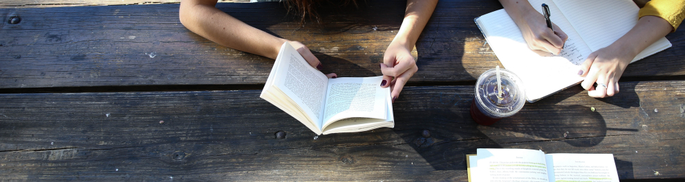 Imagem aérea de duas meninas lendo livros diferentes em uma mesa de madeira