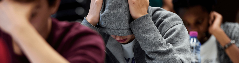 Um jovem sentado usando um casaco com capuz e com as mãos na cabeça