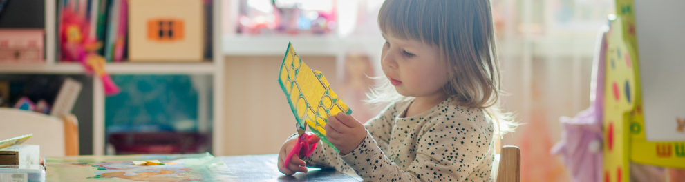 Uma menina com idade em torno de 4 anos recorta um papel.
