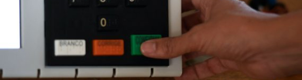 Uma pessoa apertando a tecla confirma de uma urna eletrônica