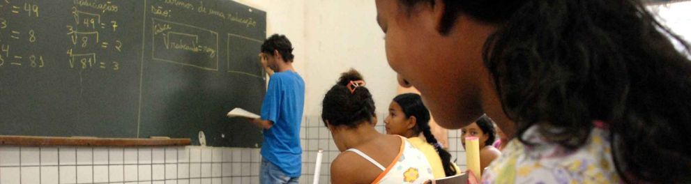 Uma sala de aula com diversos estudantes e um professor escrevendo em um quadro negro