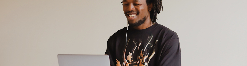 Homem negro sorridente está sentado usando um notebook à sua frente