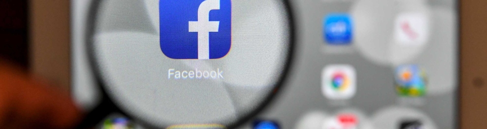A imagem mostra vários ícones de redes sociais e a do Facebook em evidência através de uma lupa