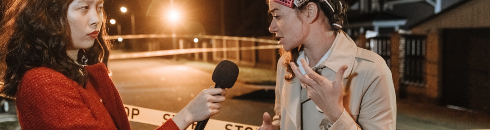 Uma repórter asiática entrevistando uma outra mulher asiática ao ar livre durante a noite