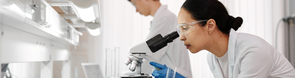 Uma cientista oriental está de perfil para quem bateu a foto e olhando algo em um microscópio