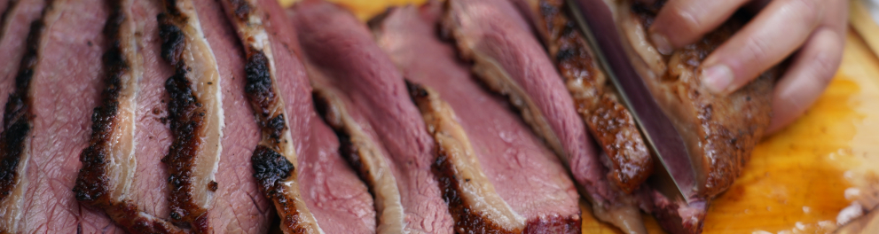 Close em uma carne mal passada sendo fatiada em uma tábua de madeira