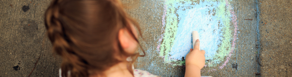 Uma menina brincando com giz colorado em um asfalto