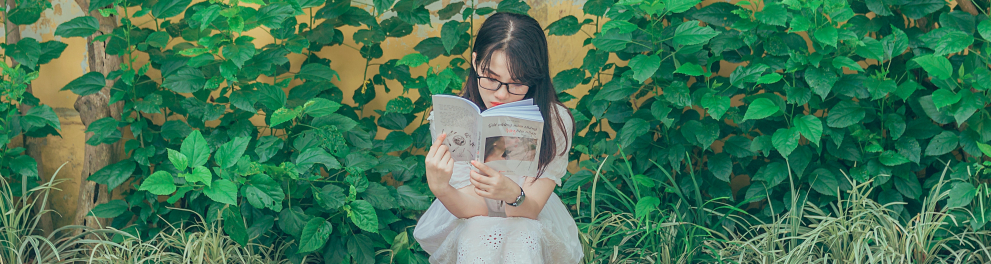 Uma jovem menina branca asiática está sentada na beira de um jardim lendo um livro