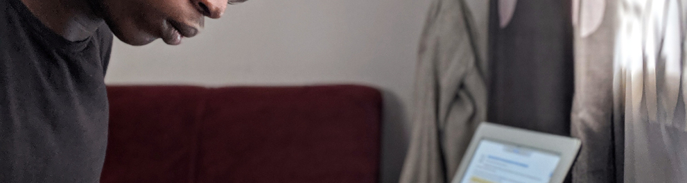 Jovem homem negro de óculos de grau está sentado de perfil para quem bateu a foto e lendo um livro com uma caneta entre os dedos da mão direita