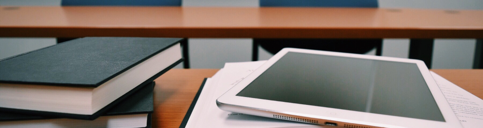 Livros e um tablet em cima de uma mesa de sala de aula