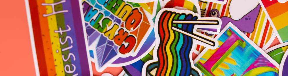 Vários adesivos do orgulho lgbtqia+ estão espalhados em uma superfície rosa