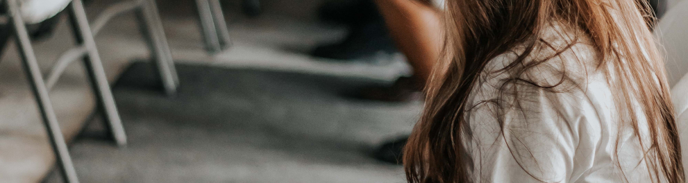 Menina loira com uniforme escolar está sentada em uma cadeira lendo um livro