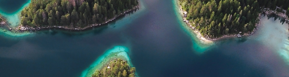 Imagem aérea de um grande lago, com vegetação bem verde ao seu redor e a água em dois tons belos de azul